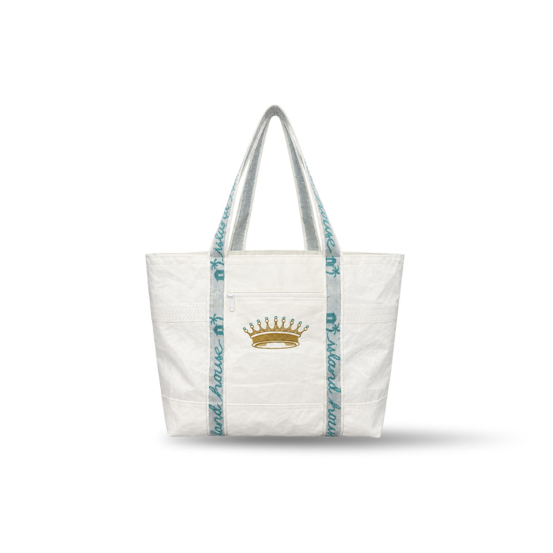 The front of a large tote made of white reclaimed sailcloth. The straps are made of sail tie webbing and are white with aqua blue lettering that reads "Island House". A gold crown is embroidered on the middle of the front with the word "STITCH" on it in aqua blue,