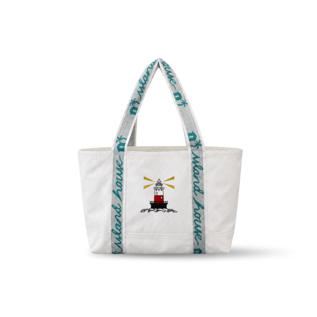 The front of a medium tote made of white reclaimed sailcloth. The straps are made of sail tie webbing and are white with aqua blue lettering that reads "Island House". A lighthouse is embroidered on the middle of the front.