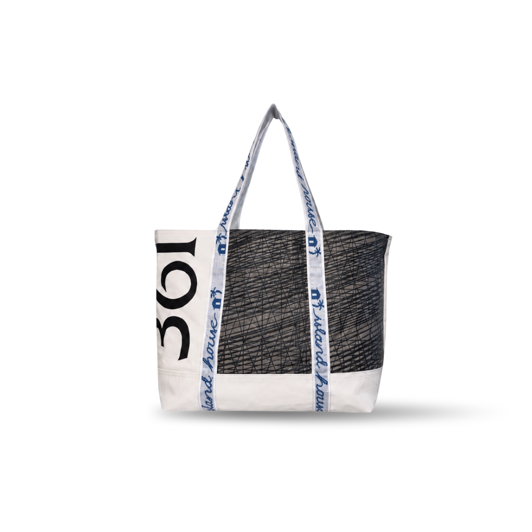 The front of a large tote made of white reclaimed sailcloth. The straps are made of sail tie webbing and are white with navy blue lettering that reads "Island House". The sailcloth features original black and gray markings, with the number 361.