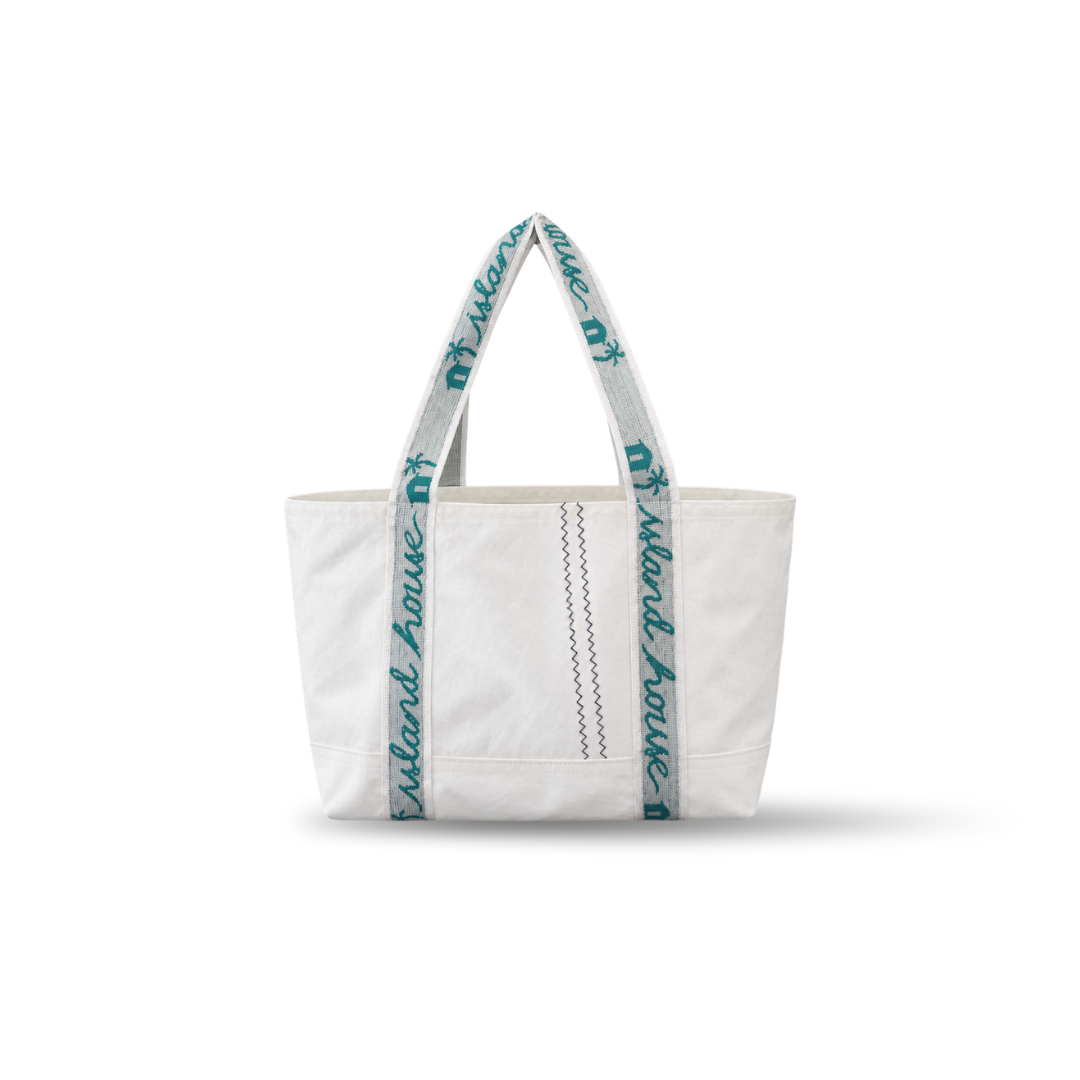 The front of a medium tote made of white reclaimed sailcloth. The straps are made of sail tie webbing and are white with aqua blue lettering that reads "Island House".
