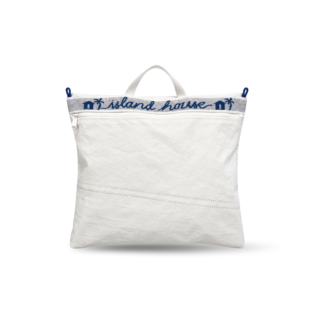 The front of a zippered project bag made of white reclaimed sailcloth. The straps are made of sail tie webbing and are white with navy blue lettering that reads "Island House".